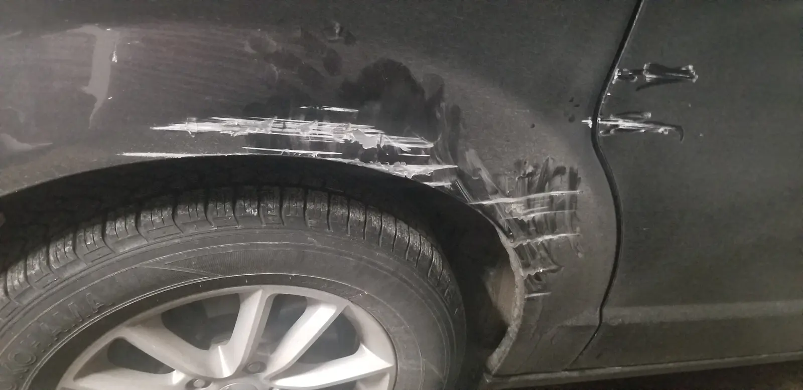 Deep scrape on a black car rear fender before repair